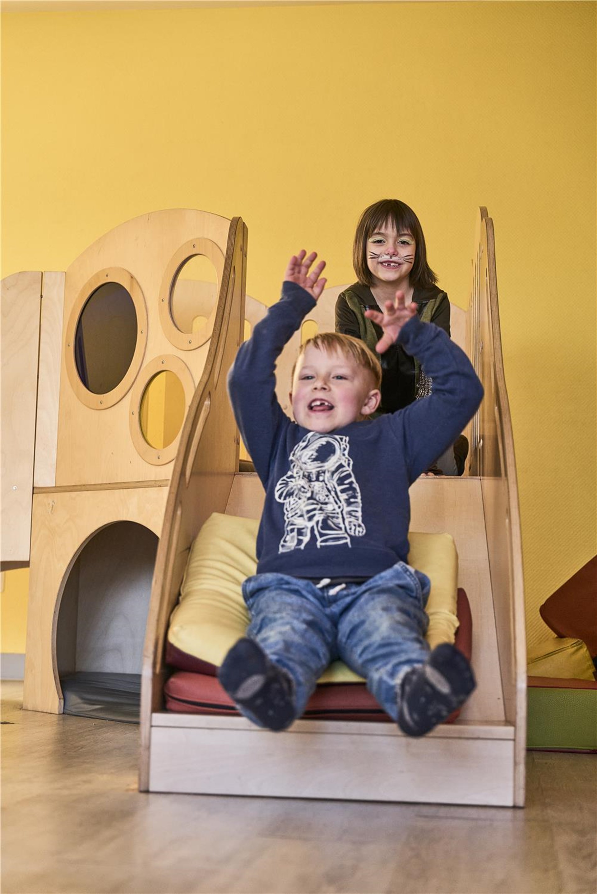 Junge und im Hintergrund Mädchen rutschen eine kleine Rutsche runter